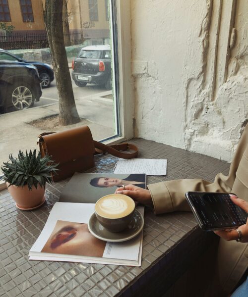 FRau sitzt in einem CAfe, trinkt Kaffee und ist am Smartphone